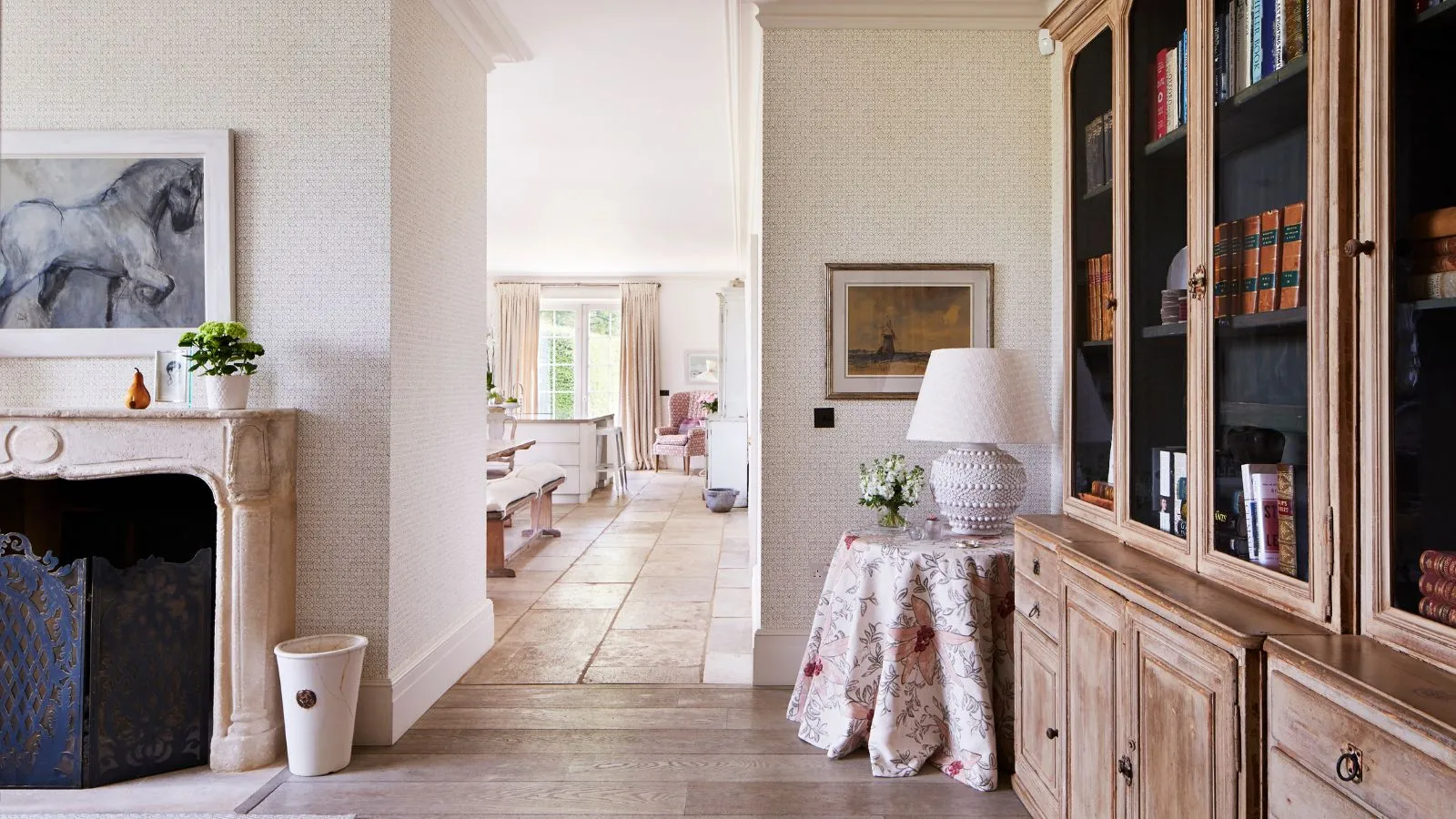 סלון מואר עם קירות לבנים ארונות עץ ומדף אבן עם יצירת אמנות של סוס מעל. מאחור מבעד למסדרון פתוח נראה מטבח עם ספסל ישיבה ואי למטבח.' loading='lazy' title=