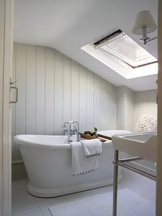 Rulltopp badekar i nøytralt bad med shiplap panel og velux vindu