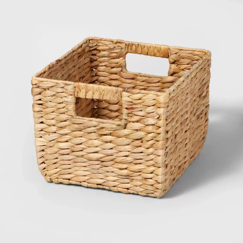 Un petit panier de rangement cubique tissé avec des poignées découpées.' loading='lazy' title=