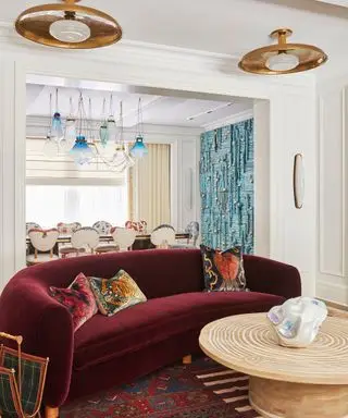 Bourgogne buet sofa i velour, placeret over et mønstret område tæppe, der indrammer et træ og afrundet sofabord