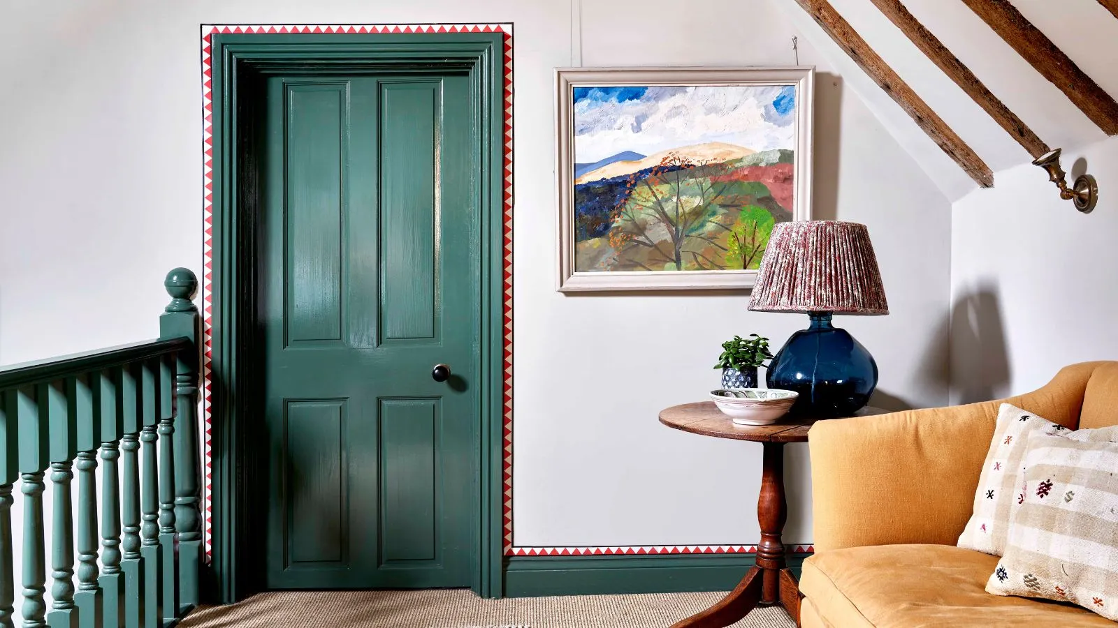 En repos i toppen af ​​en trappe med grønne gelændere og matchende grøn dør og trim. Røde detaljer malet rundt om besætningen. En gul sofa på højre side ved siden af ​​et rundt sidebord i træ med en lampe på.' loading='lazy' title=