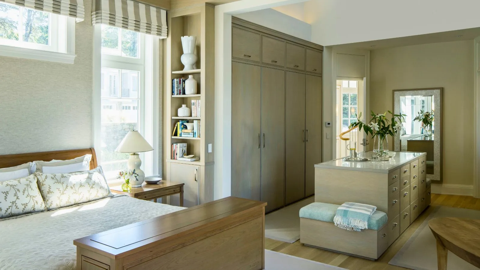 Neutralt stort soveværelse til venstre med walk in closet område til højre. Skabet har indbyggede gulv til loft skabe synlige samt en ø med skuffeopbevaring. Den naturlige indretning er beroligende og neutral med striber og blå accenter' loading='lazy' title=